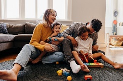 a young couple laughing and playing with their two children on the floor of their living room