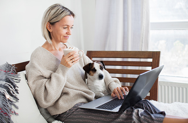 woman lounging on a couch with a cup of coffee in one hand and a laptop computer and puppy