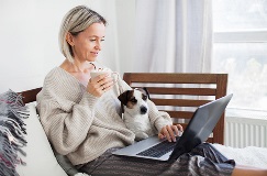 woman lounging on a couch with a cup of coffee in one hand and a laptop computer and puppy
