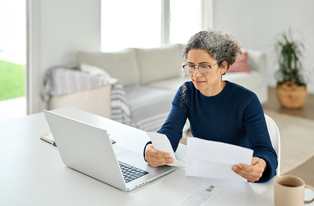 woman at a desk with a laptop reviewing paperwork and notes
