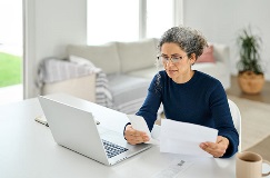 woman at a desk with a laptop reviewing paperwork and notes