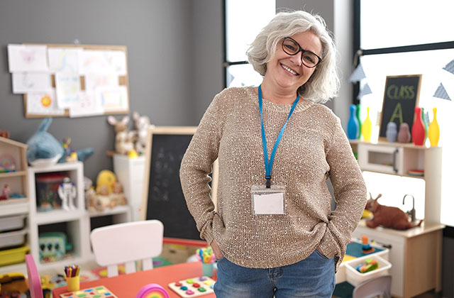 teacher standing in a classroom, smiling at camera