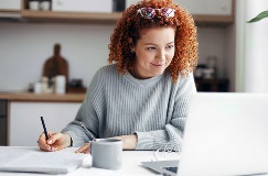 a woman using a laptop and taking notes in a notebook