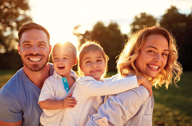 A smiling family of 4; mom, dad and two young children.