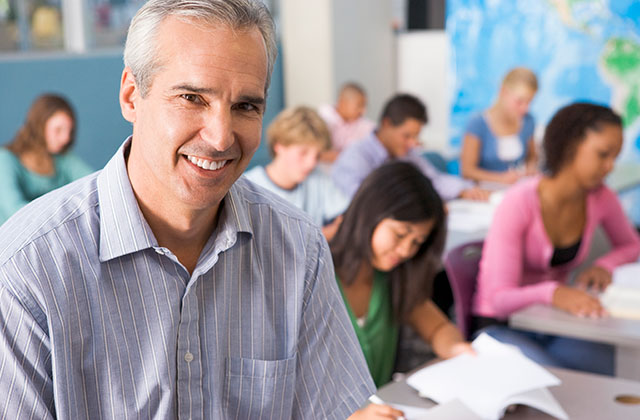 male teacher posing in front of a classroom, smiling