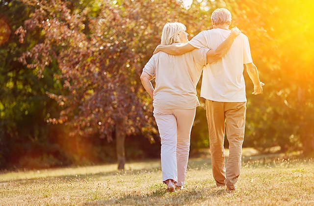 a couple walking through a forested park arm-in-arm