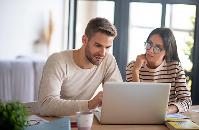 young newly married couple looking at a laptop computer together on the kitchen table