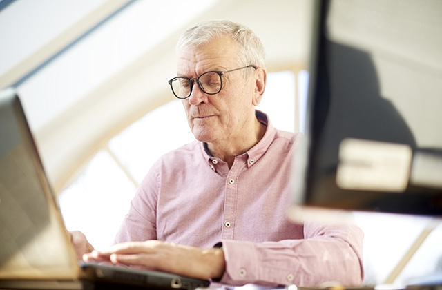 retired man sitting at a desk typing on computer keyboard