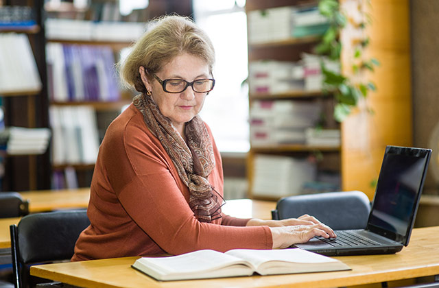 older woman typing at a  table in a library