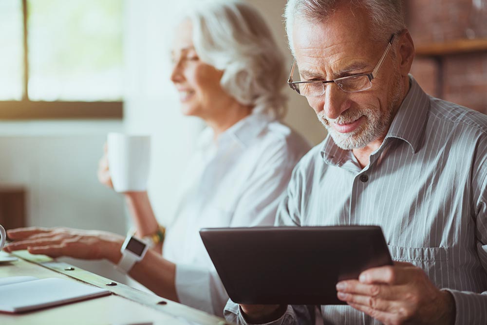 older couple sitting at a kitchen island drinking coffee and looking at a tablet device